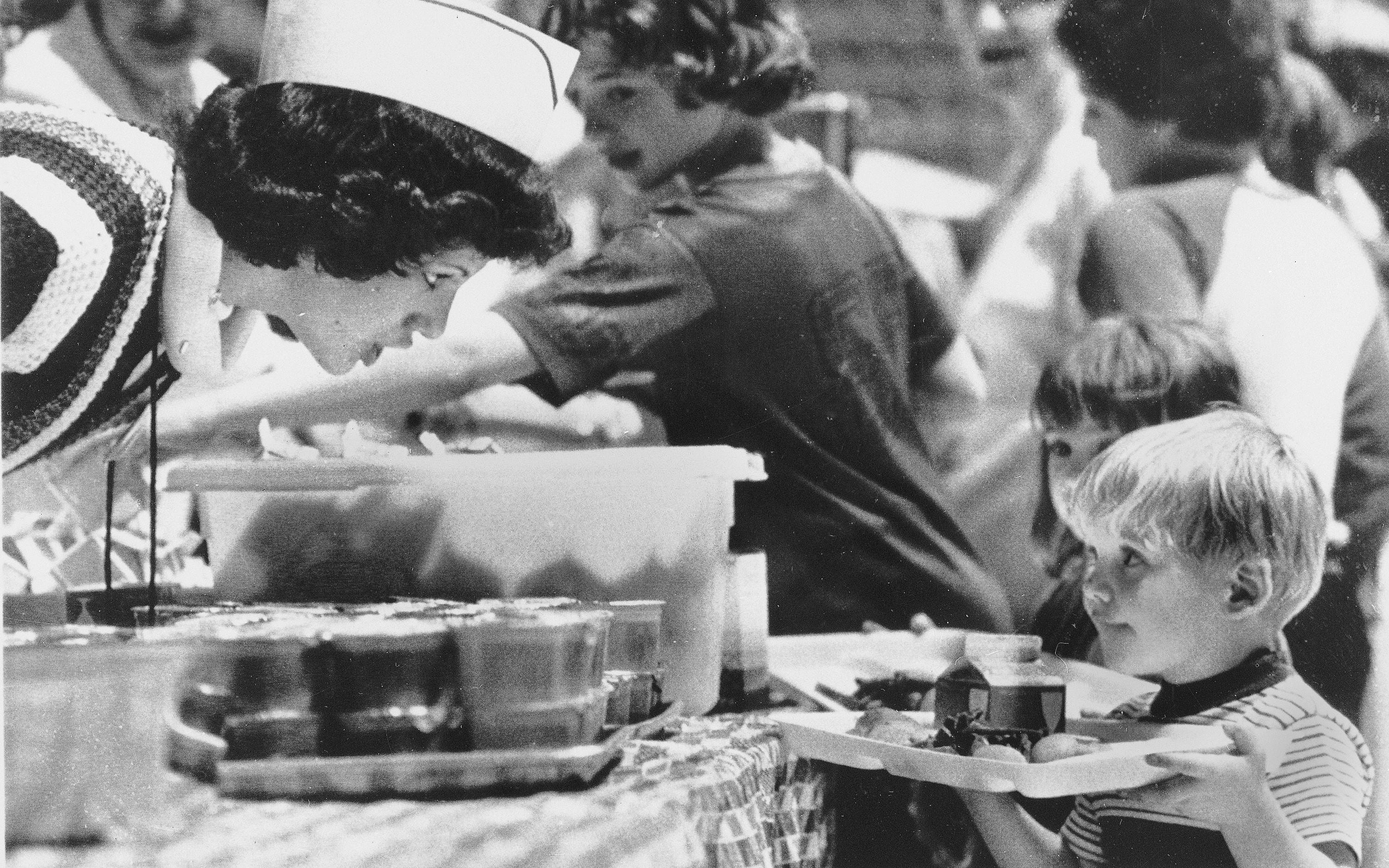 A Red Cross volunteer leans over to make sure a youngster has everything he wants for lunch at the evacuation center in Hershey Park, Pa., April 4, 1979. Expectant mothers and preschool children were asked to remain at the center for those who live within a 5-mile radius of the Three Mile Island nuclear plant. (AP Photo/Rusty Kennedy)
