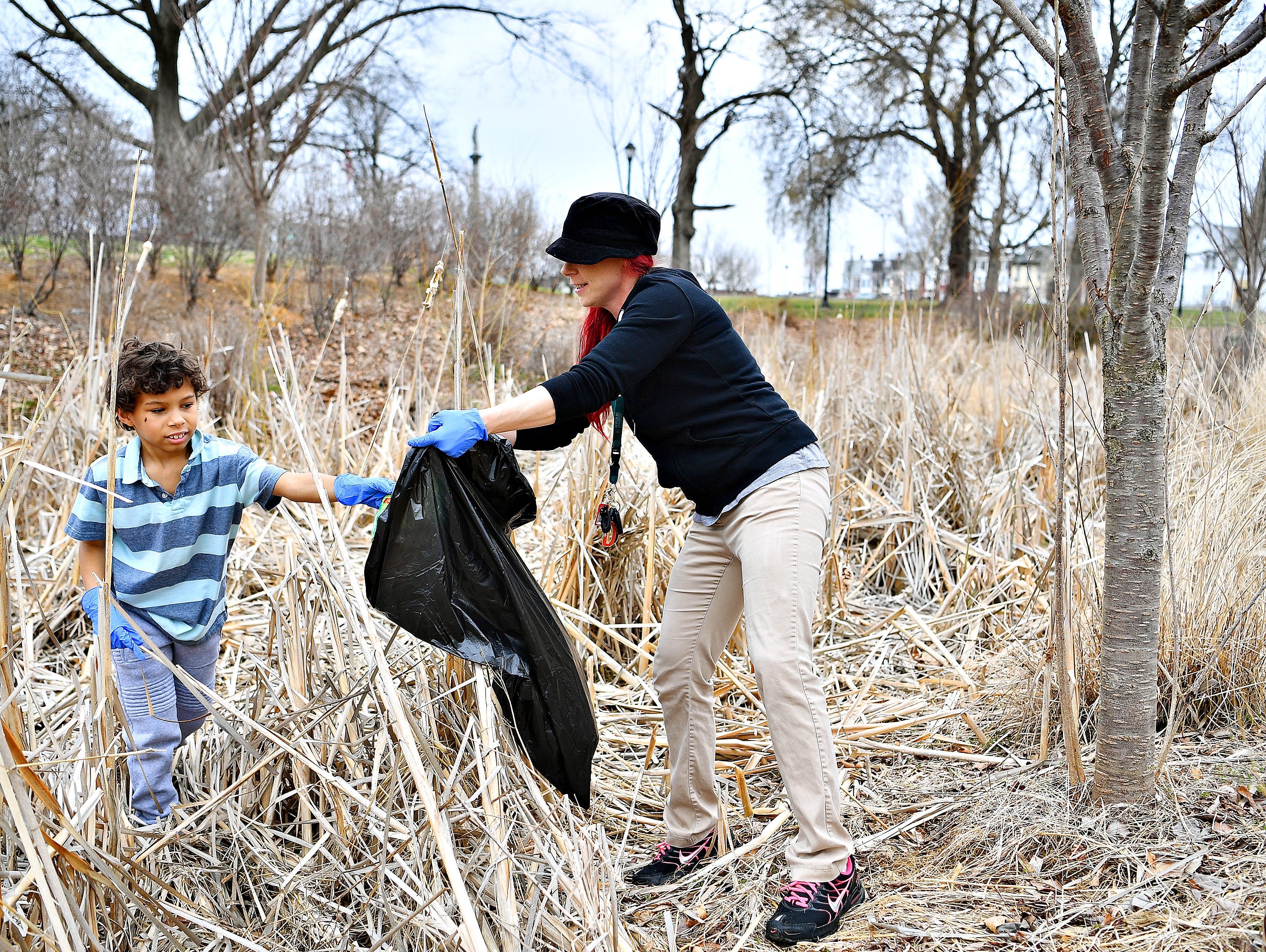 Parent liaison Destiney Boldizar, right, holds a bag out so her son, Dylan Boldizar, 8, can place trash in it as Edgar Fahs Smith STEAM Academy begins its Spring Neighborhood Cleanup at Penn Park in York City, Saturday, March 30, 2019. Dawn J. Sagert photo